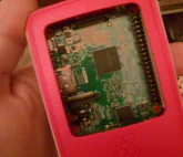 Raspberry Pi 2 in an official strawberry red and white case in the palm\nof a human hand, with top cover removed and Pi 2 circuit board showing\n