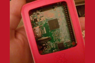 Raspberry Pi 2 in an official strawberry red and white case in the palm\nof a human hand, with top cover removed and Pi 2 circuit board showing\n